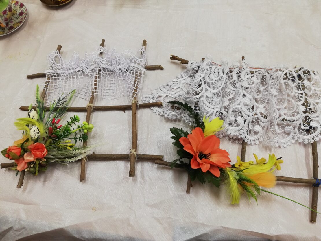 na stole leży stelaż z patyków. Na nim kilka kwiatów oraz materiałowa siatka.
